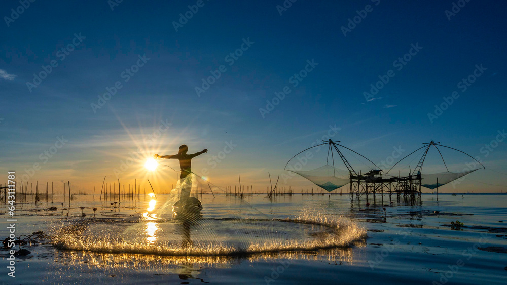 Silhouette of fisherman cast their nets to catch fish in the morning on the lake at Pakpra village, Phatthalung, Thailand