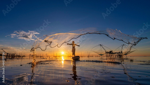 Silhouette of fisherman cast their nets to catch fish in the morning on the lake at Pakpra village, Phatthalung, Thailand