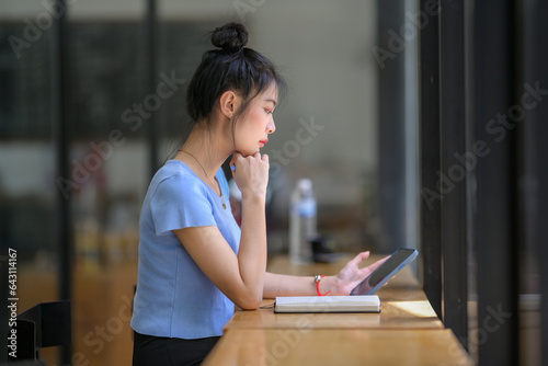 A young Asian woman sitting in a coffee shop using her smartphone to search for information inspires new ideas.