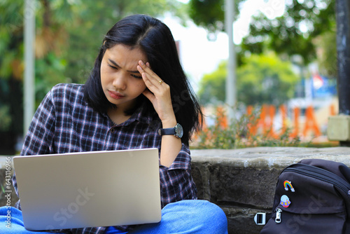 exhausted and stressed asian woman student working using laptop and study with text books in outdoors