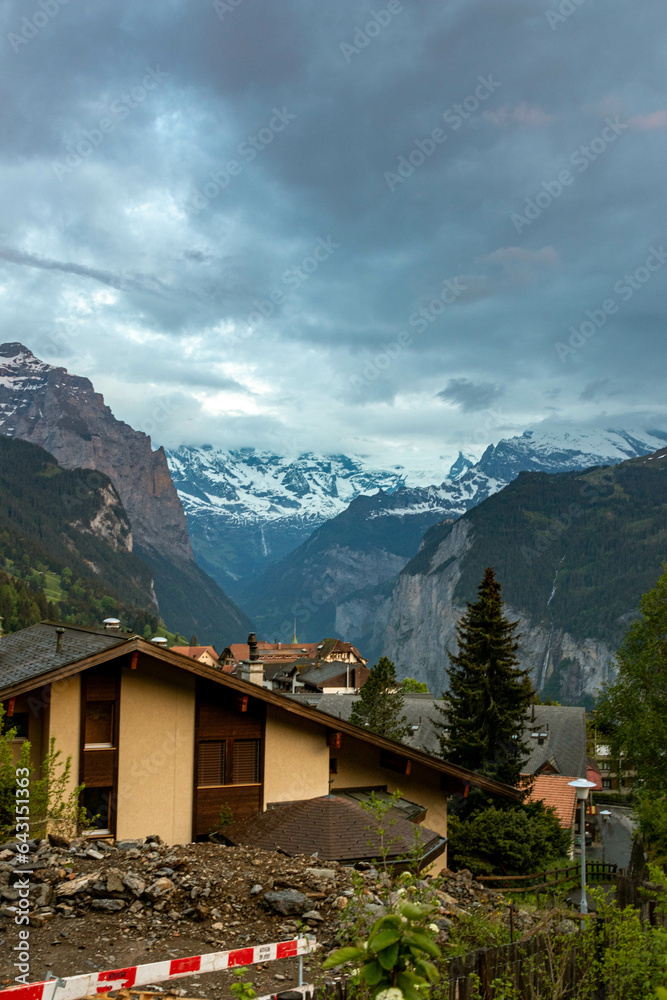 The Swiss Alps with Buildings Sitting Along the Hills and Mountains in the background in Switzerland in Summer The Swiss Alps with Buildings Sitting Along the Hills and Mountains in the background in Switzerland in Summer