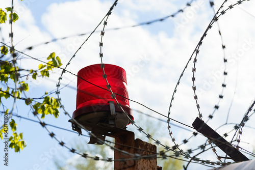 A fence with barbed wire and a red flasher against a sky with clouds. photo