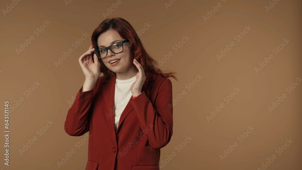 Medium isolated shot of a satisfied, shy and relaxed young woman fixing the glasses she is wearing, looking at the camera smiling.