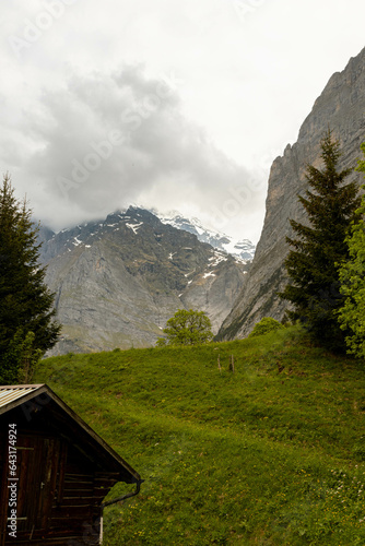 Buildings Sitting Along a Hill of the Swiss Alps in Switzerland in the Summer with Mountains Peaking Through Clouds in the Background