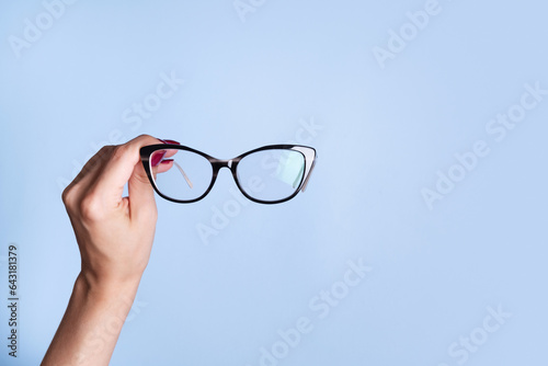 Eyeglasses in female hand on blue background. Optical store, vision test, stylish glasses concept