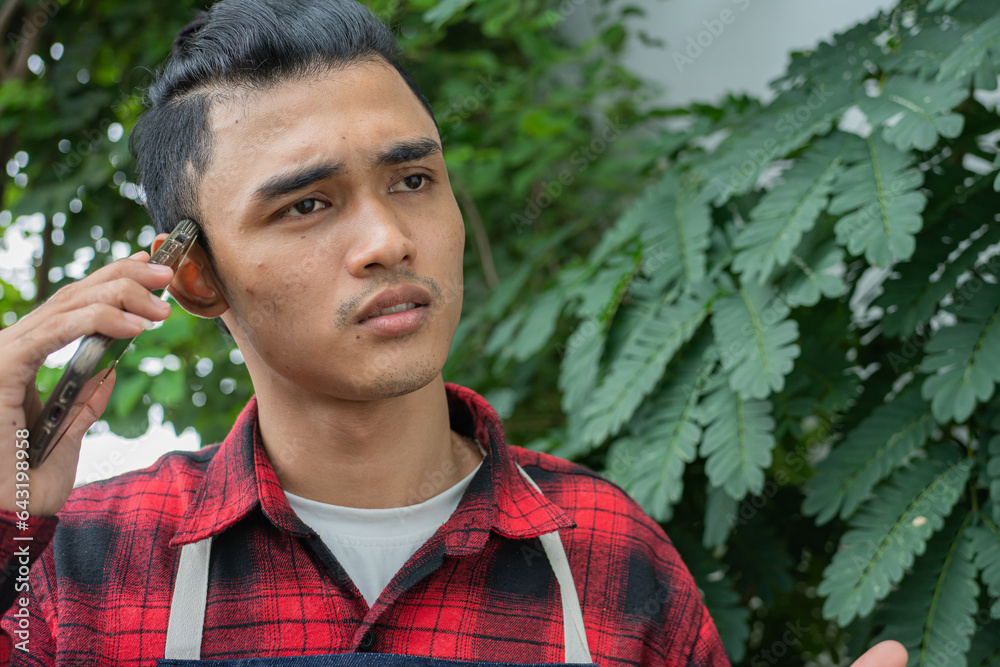Asian young man Wearing a red and black plaid shirt, wearing a denim apron. Has a stressed expression while talking on the phone