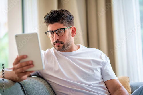 Close-up of a middle-aged man sitting at home on the sofa and holding a digital tablet in his hand photo