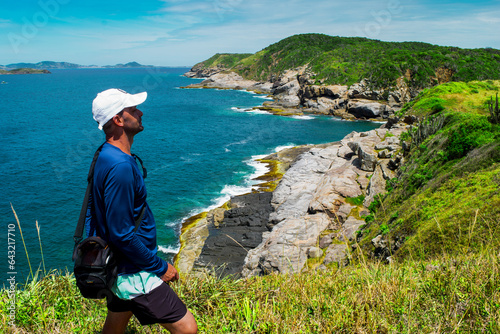 Man enjoying a view from above of the beautiful Praia das Conchas, near the city of Cabo Frio, with blue sea around, undergrowth, large rocks and mountains in the background - 80