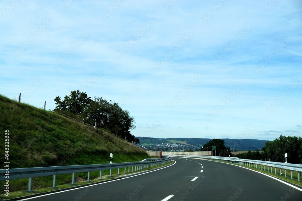 Kurvige Landstraße zwischen grüner Landschaft vor Himmel bei Sonne am Nachmittag im Sommer Kurvige Landstraße zwischen grüner Landschaft vor Himmel bei Sonne am Nachmittag im Sommer