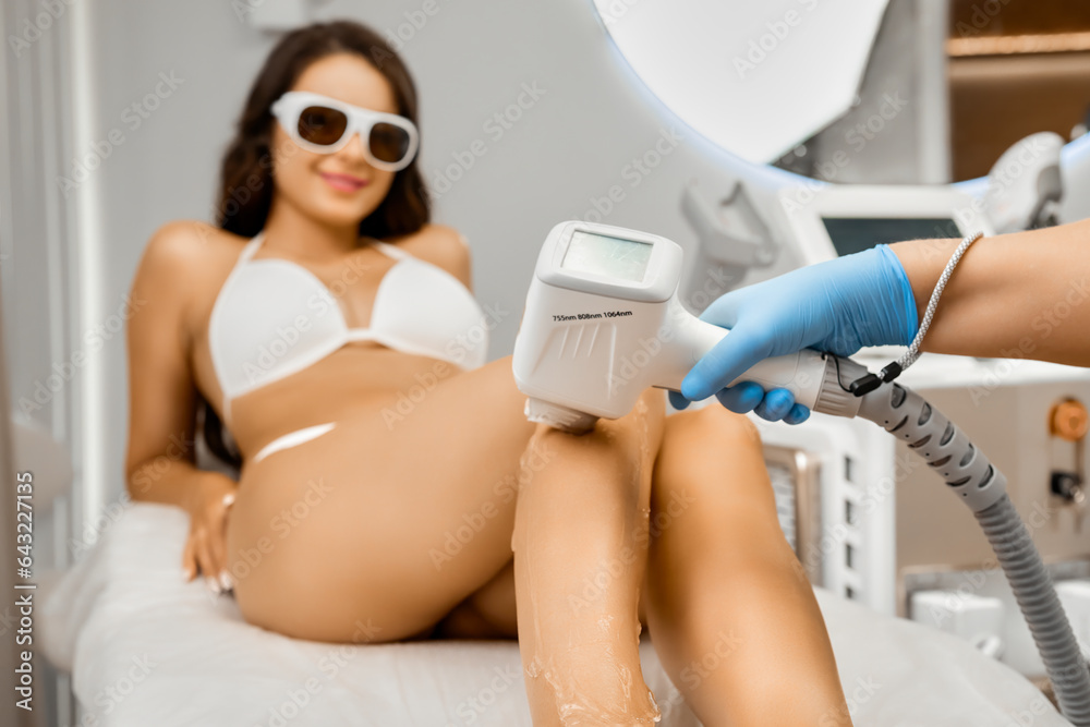 Laser epilation procedure for happy young woman in protective goggles and bikini in clinic center.