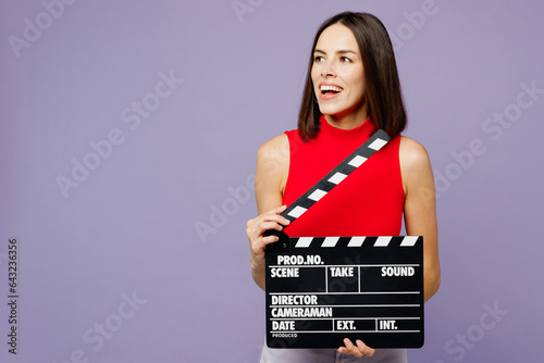 Young woman she wears red tank shirt casual clothes hold in hand classic black film making clapperboard look aside isolated on plain pastel light purple background studio portrait. Lifestyle concept.