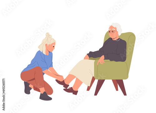 Young woman volunteer helping elderly female sitting on armchair to put on shoes isolated on white