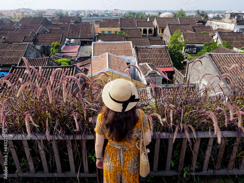 Vietnamese female tourist looks at the ancient rooftops in Hoi An ancient town (Vietnam) from a high-rise cafe photo