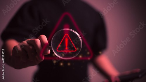 Hand holding magnifier glass with red triangle caution warning sign for focus notification error and maintenance concept. photo