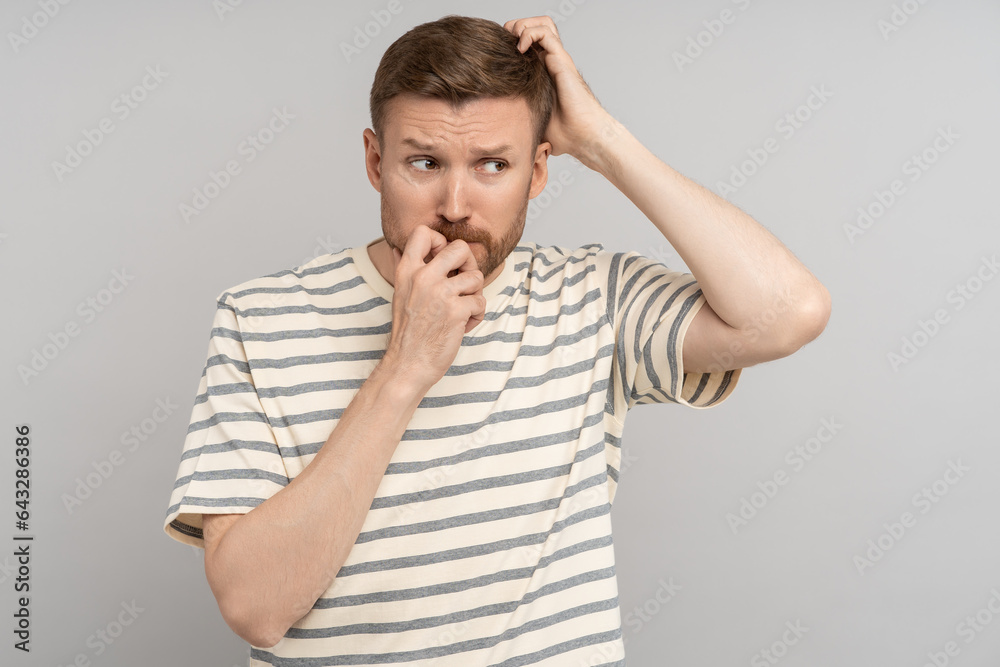 Nervous guy with mental health disorder in difficult thought scratches back of head, bites nails, looking away, isolated background. Worried man with shame signs of an unstable psyche afraid exposure. Nervous guy with mental health disorder in difficult thought scratches back of head, bites nails, looking away, isolated background. Worried man with shame signs of an unstable psyche afraid exposure.