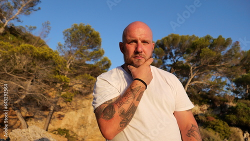 sychev, Portrait of a bald brutal man with beard and tatoo and blue eyes dressed in a t-shirt white by the Mediterranean Sea, France photo