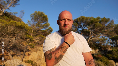 sychev, Portrait of a bald brutal man with beard and tatoo and blue eyes dressed in a t-shirt white by the Mediterranean Sea, France photo