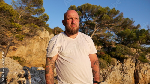 sychev, Portrait of a bald brutal man with beard and tatoo and blue eyes dressed in a t-shirt white by the Mediterranean Sea, France photo