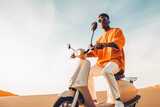 Young black man in sport clothes and sunglasses driving scooter