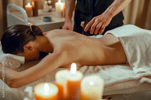 Masseur man therapist pouring warm herb infused oil on female back.