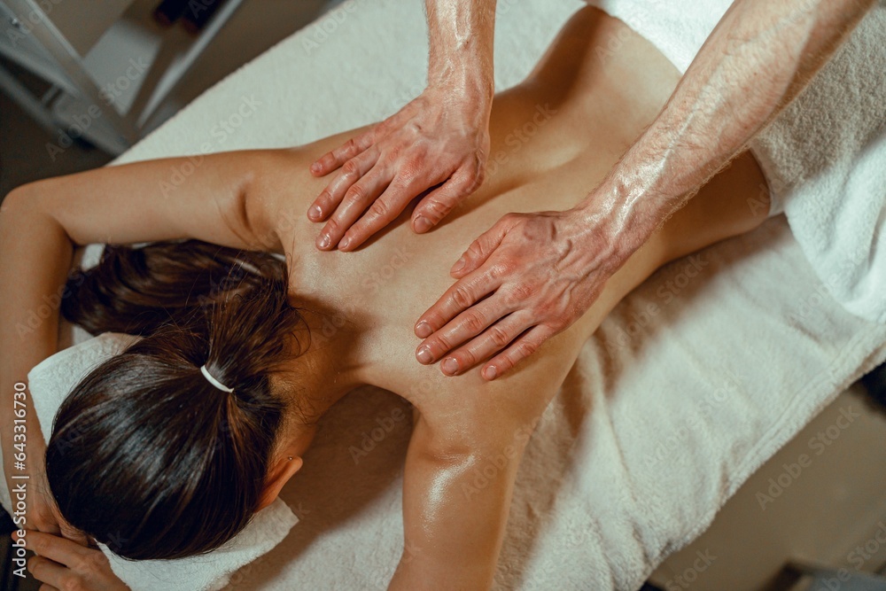 Top view masseur man doing back massage using oil to a woman in spa salon. Therapy, resort Top view masseur man doing back massage using oil to a woman in spa salon. Therapy, resort