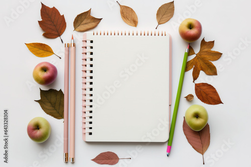 On a white background, a notepad has pencils, apples, and leaves from the fall. returning to school idea. On a desk with space for copies are office supplies. I'll go back to my schooldays