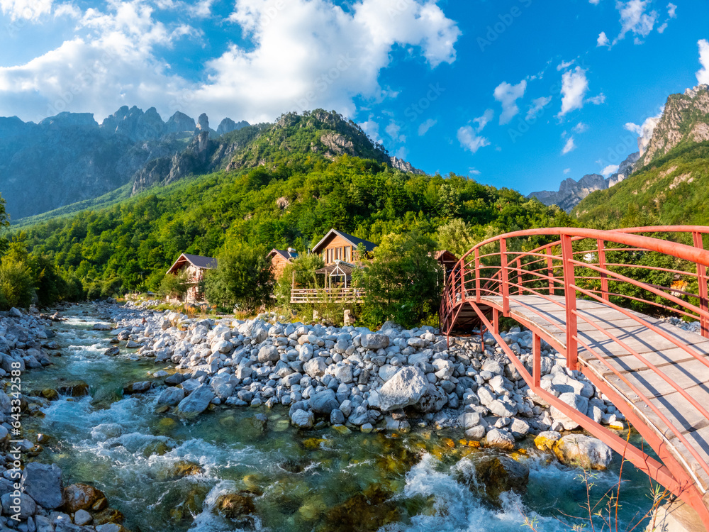 Red bridge along the river of Valbona Valley and some wooden houses or lodges, Theth National Park, Albanian Alps, Albania - obrazy, fototapety, plakaty 