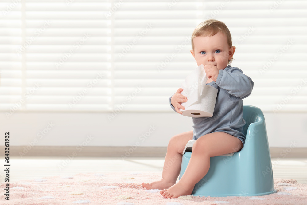 Little child with toilet paper roll sitting on plastic baby potty indoors. Space for text Little child with toilet paper roll sitting on plastic baby potty indoors. Space for text