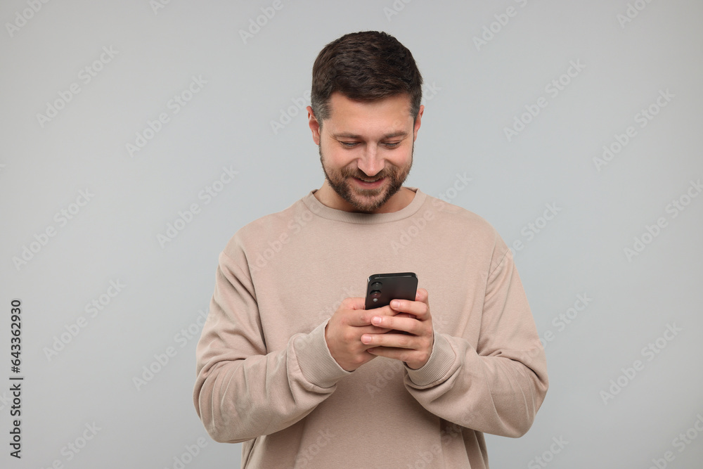 Happy man using smartphone on light grey background Happy man using smartphone on light grey background