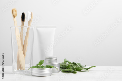 Toothbrushes, dental products and herbs on white wooden table. Space for text