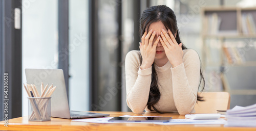 Stressed business asian woman working from at workplace on laptop looking worried, tired and overwhelmed and migraine attack. Tired asian Freelance, work. photo