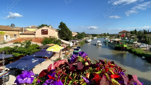 View from the historic bridge with flower decorations on the Canal du midi near Le Somail, summer, sun, blue bumblebee, tourist boat sails on the canal, restaurant on the bank, Departement Aude photo