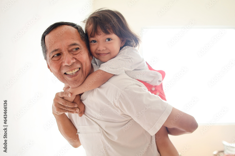 Grandfather carrying his granddaughter on his back at home Grandfather carrying his granddaughter on his back at home