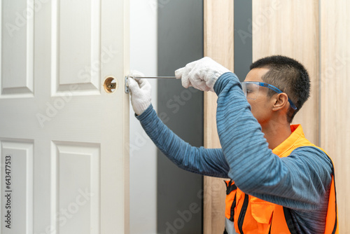 Asian professional locksmith installing or repairing a door knob with screw drive or cordless drill.