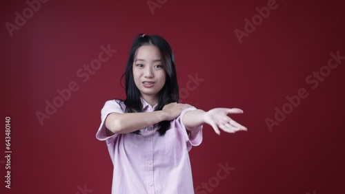 A Indonesian girl wearing a casual pink shirt, dancing macarena. Isolated on a maroon background.