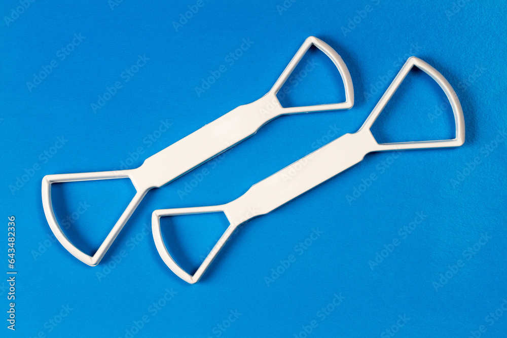 Two universal scrapers for cleaning the tongue on a blue background. Personal hygiene products. White plastic scrapers for cleaning the tongue. Two universal scrapers for cleaning the tongue on a blue background. Personal hygiene products. White plastic scrapers for cleaning the tongue.