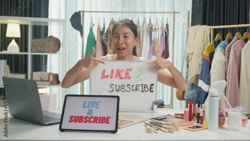 Young Asia lady beauty blogger wear crop top hold whiteboard smile looking at camera live stream talk follower introduce her chanel ask audience like subscribe share her chanel at house studio.