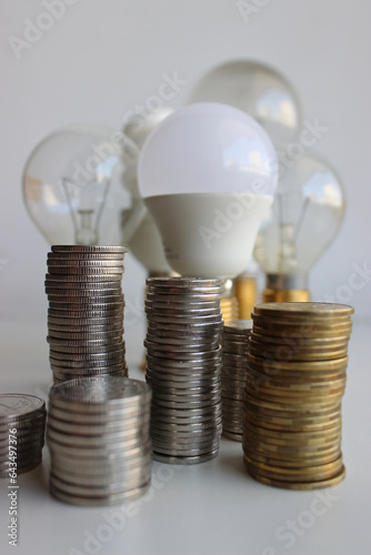 Variety Electric Bulbs And Piles Of Silvery And Brass Coins In A Columns Symbolizing Energy Efficient 
