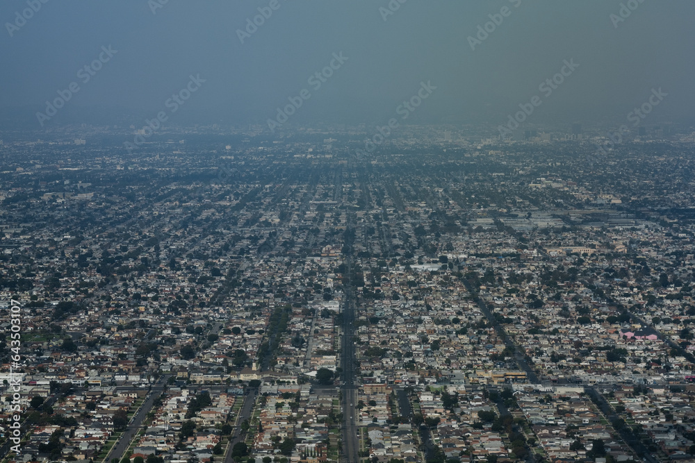 Flying low over the urban sprawl of homes in Los Angeles, a view of the cityscape as seen from a plane flying into LAX. The urban grid extends into the distance and the haze of air pollution.