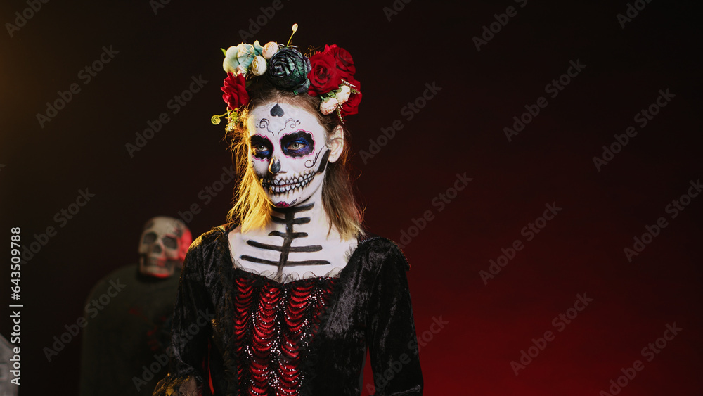 Holy goddess of death posing in halloween costume with skull make up to celebrate dios de los muertos on mexican holiday. Spooky woman as santa muerte with black and white body art. Handheld shot.