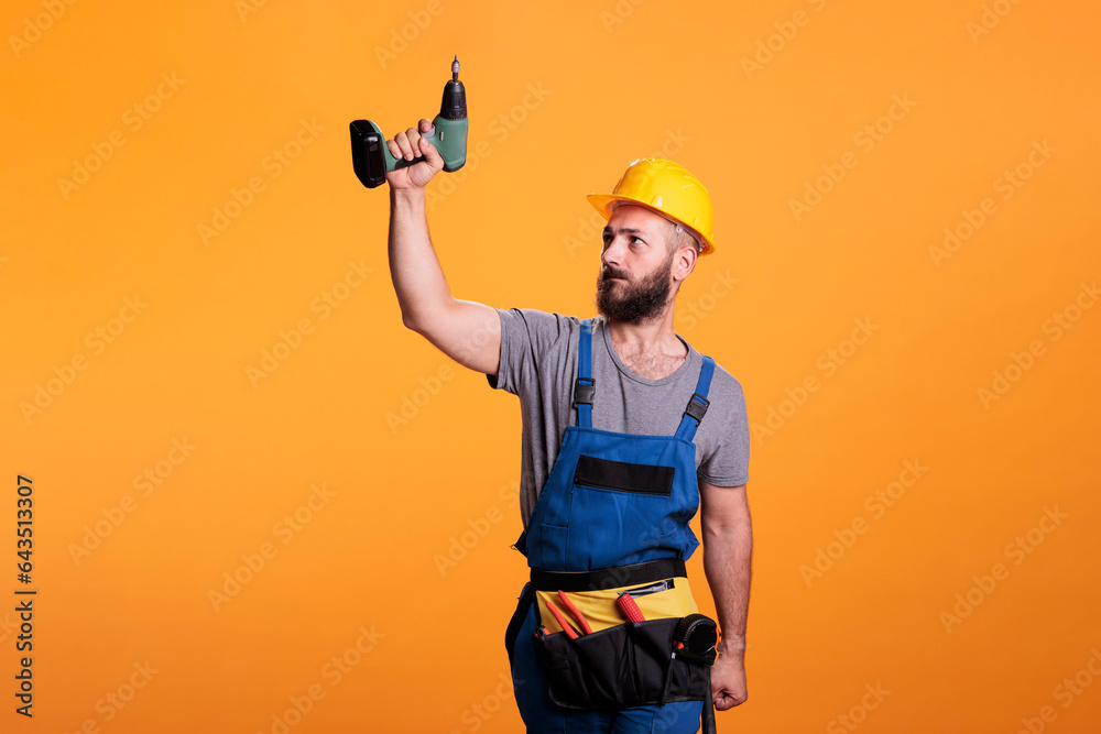 Young carpenter working wtih electric power drill tool, wearing overalls and holding drilling gun. Handyman contractor using cordless drill to work on renovation and refurbishment.