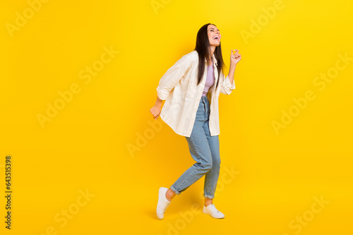 Full size photo of adorable funky positive girl wear white shirt denim trousers dancing having fun isolated on yellow color background