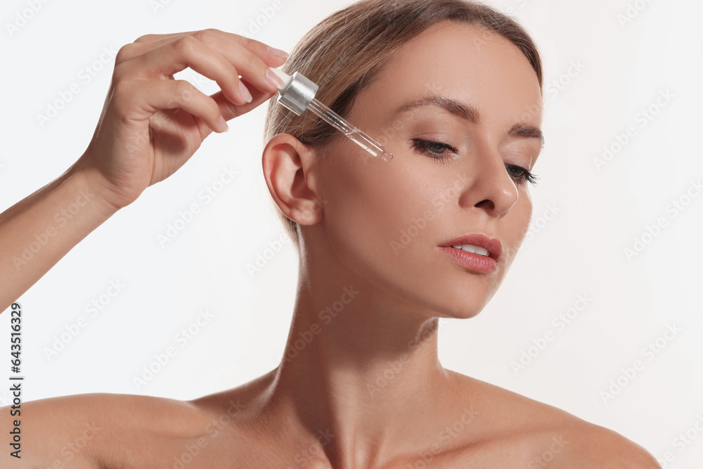 Beautiful woman applying cosmetic serum onto her face on white background