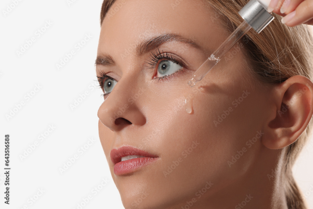 Beautiful woman applying cosmetic serum onto her face on white background, closeup