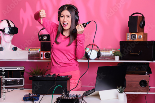 Unhappy artist holding microphone while doing disagreement gesture  expressing disagreement in studio over pink background. Dj woman performing song with electronics equipment and audio instrument