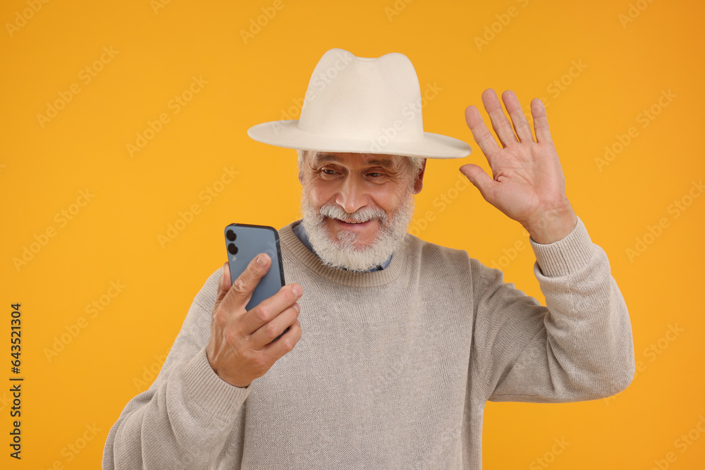 Happy senior man with smartphone having video chat on yellow background Happy senior man with smartphone having video chat on yellow background