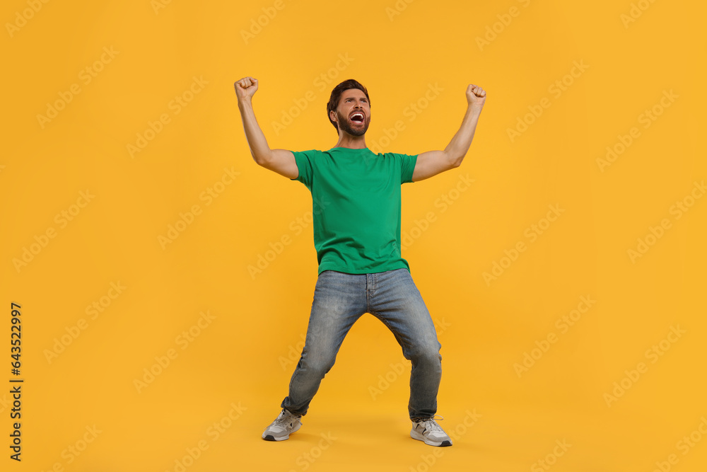 Emotional sports fan celebrating on orange background