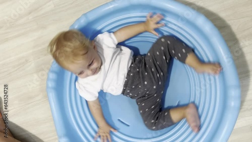 Little child playing on gymboree play. Baby spinning on blue plastic circle and having fun. Good joyful mood.