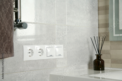 Light switches and power sockets on light grey wall in bathroom. Space for text