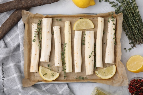 Baking tray with raw salsify roots, lemon and thyme on white marble table, flat lay photo